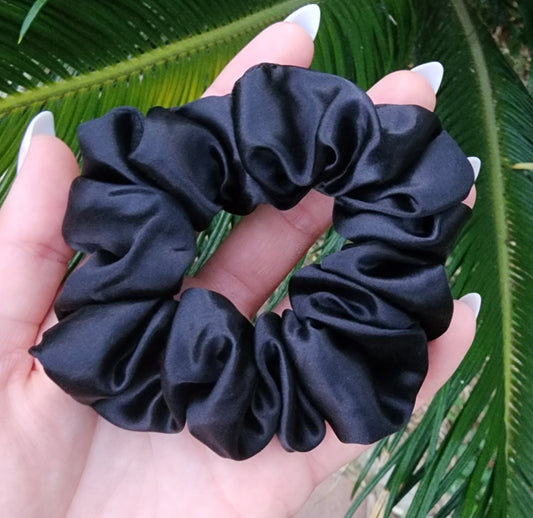 Onyx classic mulberry silk scrunchie in black held in a hand against green palm leaves