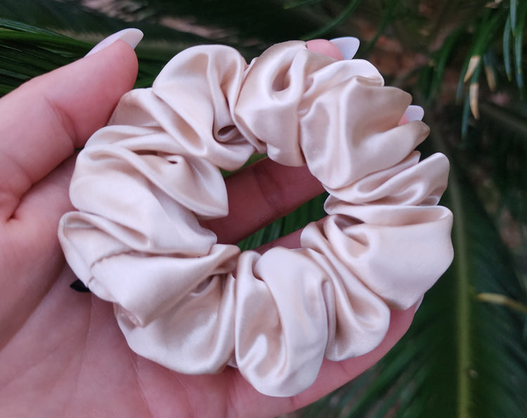 Oat Milk Classic mulberry silk scrunchie held against green palm leaves