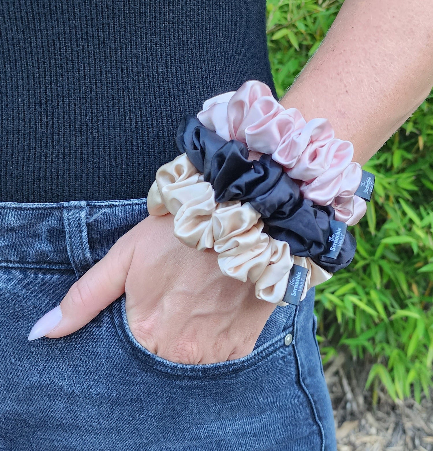 Woman wearing three classic 3.5cm Mulberry silk scrunchies in blush, black, and champagne on her wrist. Hair-safe silk accessories by The Scrunchie Vault.