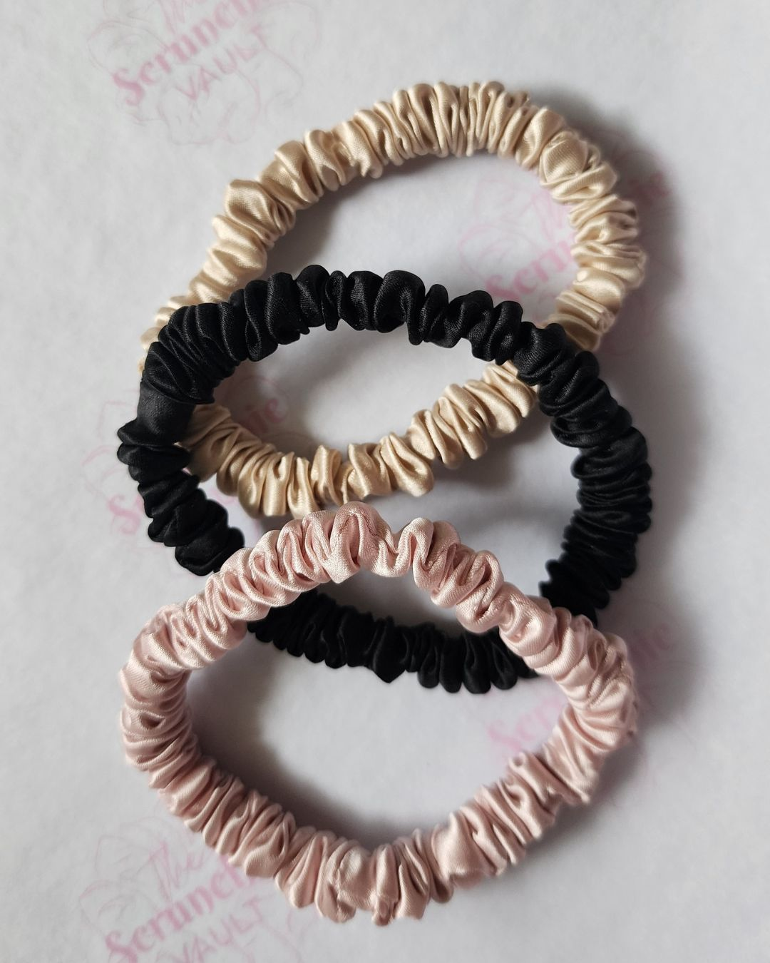 Three thin Mulberry silk scrunchies in blush pink, black, and champagne gold. Lightweight silk skinnies by The Scrunchie Vault for gentle, everyday styling.
