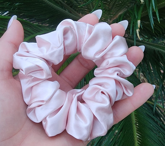 Sugar Kiss classic mulberry silk scrunchie in soft pink held in a hand against green palm leaves