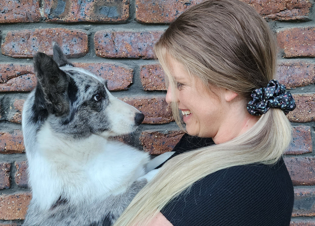 Little Paws classic mulberry silk scrunchie in dark paw print worn in a ponytail beside a black-and-white dog