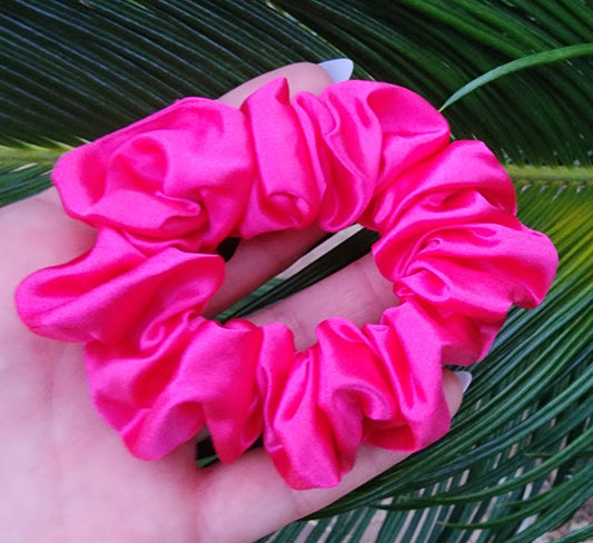 Wildberry classic mulberry silk scrunchie in hot pink held in a hand against green palm leaves