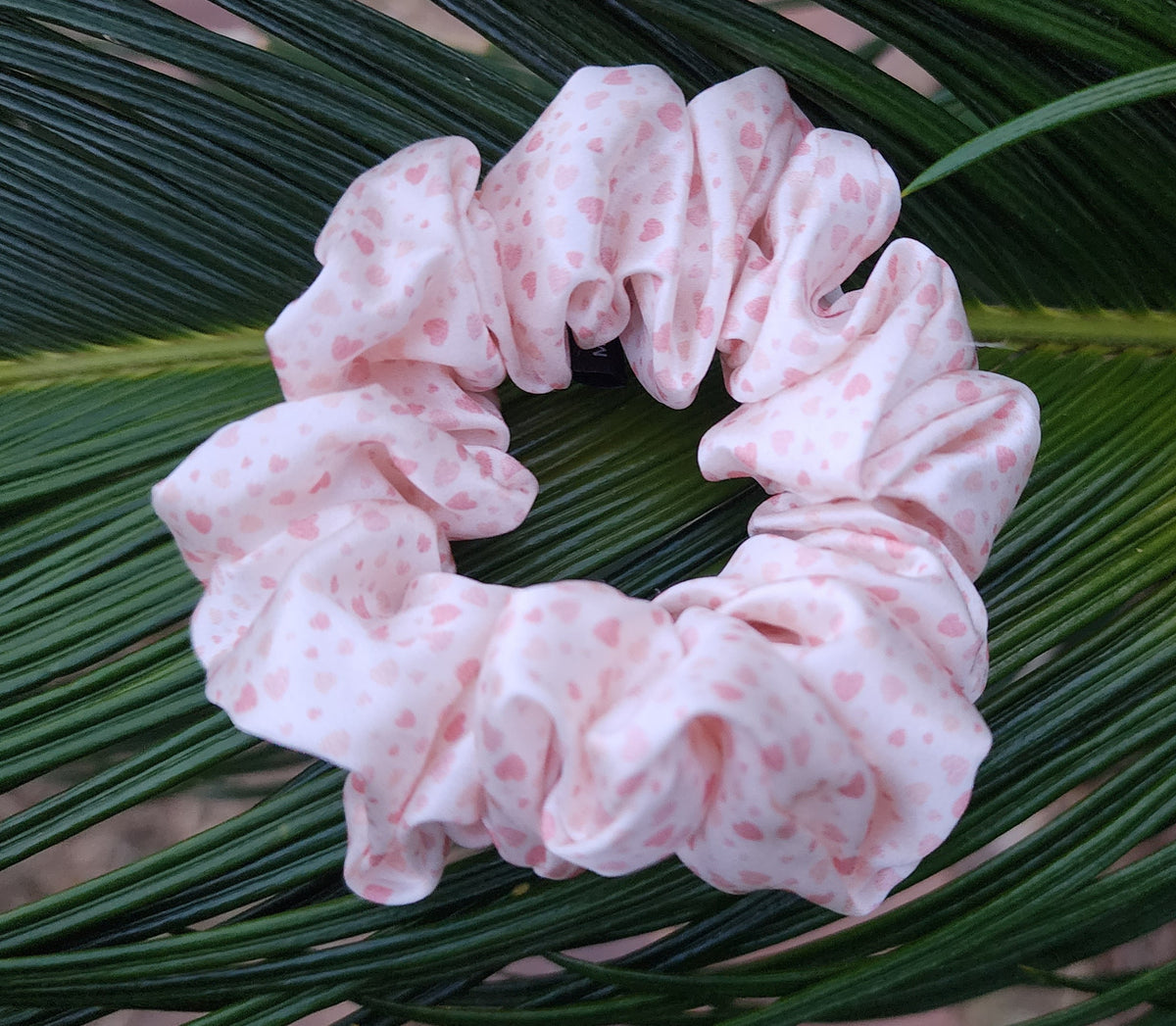 Sweetheart classic mulberry silk scrunchie in pink and white heart print resting on green palm leaves