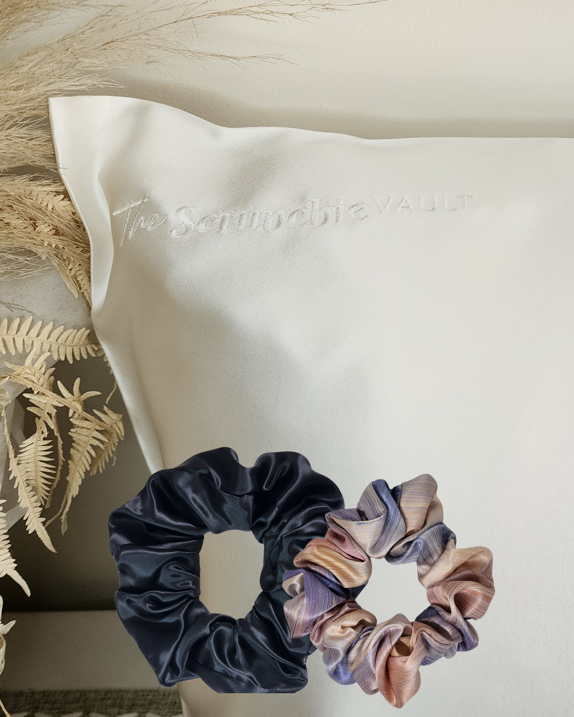 Silk Indulgence Pack – lifestyle image showing corner of 22 momme Mulberry Silk pillowcase with logo visible, classic printed scrunchie and oversized plain scrunchie in front.